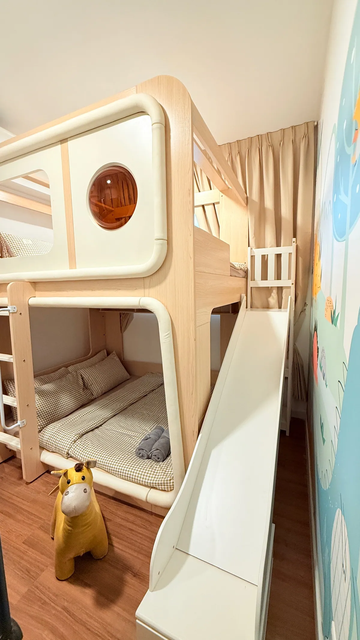 The kids' room at Kidtastic Stay KL: the bunk house with its round window, the slide and a ride-on giraffe.